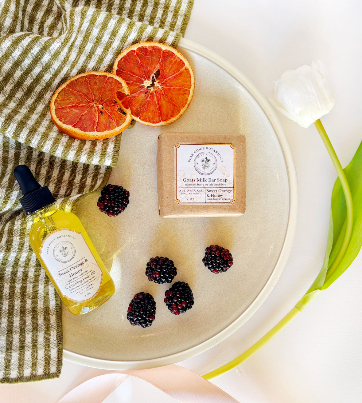Bar of soap, bottle of oil, and dried oranges on a white plate with a striped cloth.